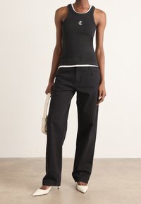 Svart linne med vit kant, med en logo, parat med lösa svarta jeans och vita spetsiga klackar. Slingrande tyg med en figurnära design.