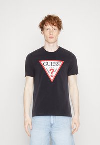 Svart bomull T-skjorte med en rød og hvit trekantet grafikk med 'GUESS®' og tekst. Kortermet og med rund halsdesign.