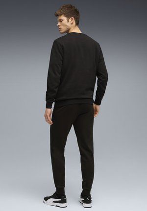 Svart sweatshirt och matchande joggers i mjukt tyg, med ribbade muddar, rund halsringning och svarta och vita sneakers.