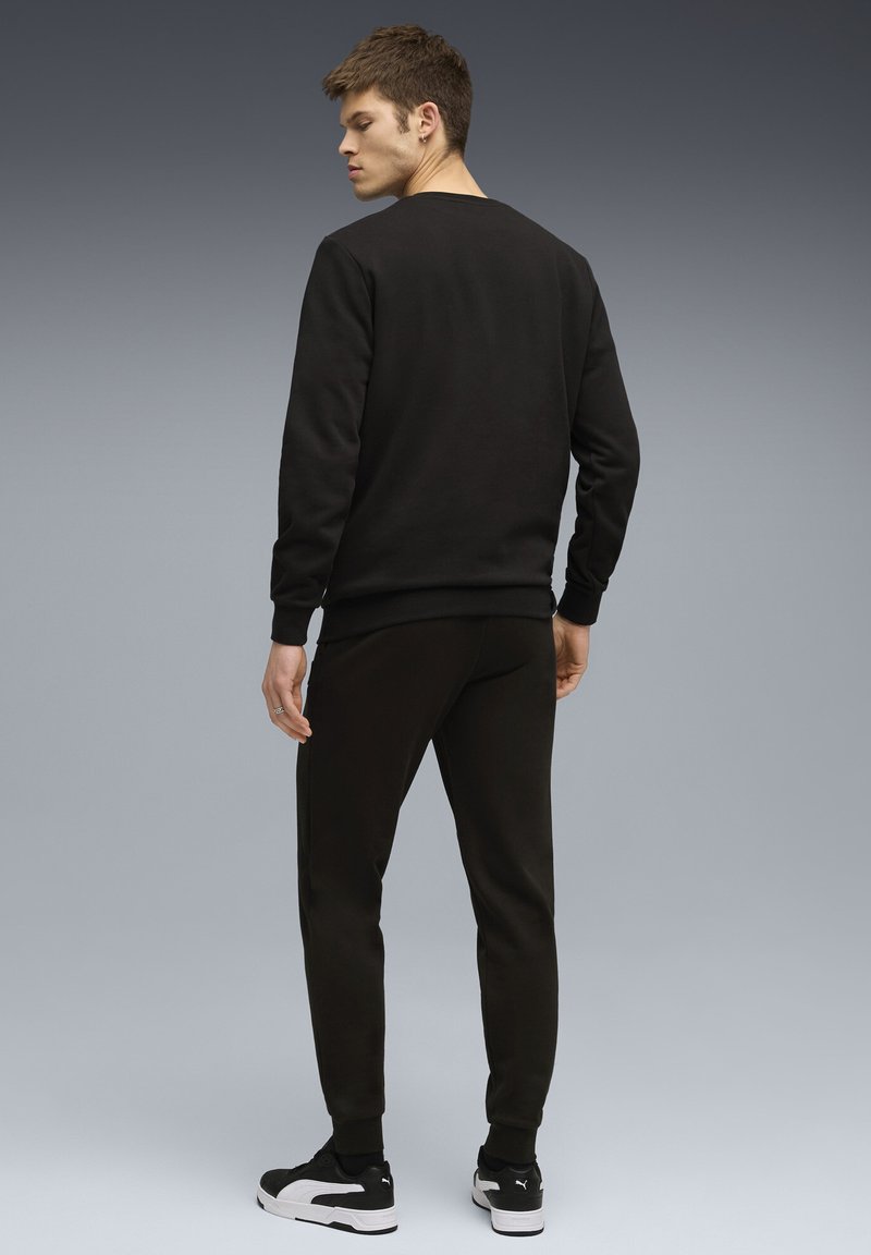 Sort sweatshirt og matchende joggers lavet af blødt stof, med ribbede manchetter, en rund halsudskæring og sort-hvide sneakers.