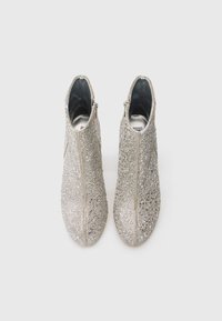 Par de botas de tobillo plateadas cubiertas de pequeños rhinestones, vistas desde arriba sobre un fondo blanco liso.