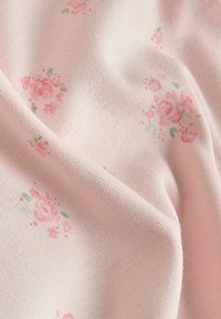 Lyserødt stof med et blomsterprint, der indeholder små roser i nuancer af pink og grønt. Blød tekstur med en fin strikket vævning.