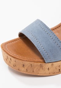Sandale compensée marron avec semelle en liège et large bride en daim bleu clair sur le dessus du pied.