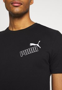Camiseta de algodón negra con un logo y emblema blancos de "PUMA". Diseño de cuello redondo con mangas cortas y una silueta ajustada.