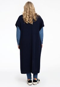 Długi granatowy sweter kardigan z dzianiny z krótkimi rękawami. Noszony na jasnoniebieską koszulę dżinsową, w połączeniu z ciemnymi dżinsami i czarnymi trampkami.