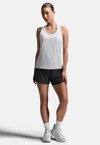 Hvid atletisk tanktop kombineret med sorte shorts. Tanktoppen har rund halsudskæring og en figursyet pasform, lavet af letvægtsstof.