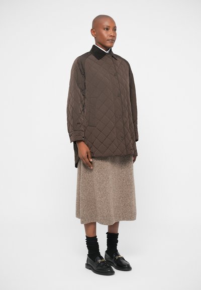 Casaco castanho acolchoado com colarinho, combinado com uma saia longa bege. Meias pretas e sapatos loafers com detalhe em corrente completam o conjunto.