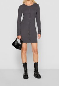 Mörkgrå, långärmad knappklänning med rund halsringning; tillsammans med svarta ankelstövlar och en liten svart handväska.