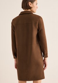 Abito marrone a maniche lunghe realizzato in tessuto morbido con colletto. Presenta un design semplice, cuciture visibili e polsini con bottoni.