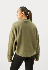Pullover in pile verde oliva con colletto alto, vestibilità ampia e texture a coste; presenta spalle scese e orlo arrotondato.