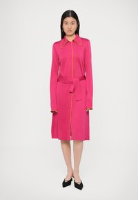 Fuksijos spalvos suknelė iš lygaus audinio, su apykakle, sagų užsegimu, liemens dirželiu ir kontrastingais geltonais akcentais palei kraštus.