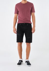 Camiseta de manga corta color burdeos con cuello redondo, pantalones cortos de mezclilla negros con detalles desgastados, combinados con zapatillas blancas y negras.
