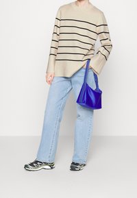 Beige gestreepte trui met zwarte strepen, relaxed fit; lichtblauwe denim jeans; kleine blauw handtas; zwarte en groene sportschoenen.