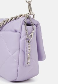 Lilla quiltet håndtaske lavet af glat materiale, med en sølv kædetraspe og et logomærke med "STEVE MADDEN" præget på.