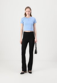 Un tricou scurt, de culoare albastru deschis, cu mâneci scurte, asortat cu pantaloni negri evazați, cu talie înaltă, și pantofi negri cu vârful ascuțit.