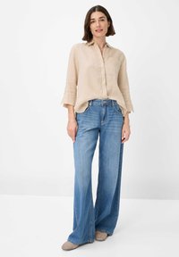 Light beige linen shirt with a collar and elbow-length sleeves, paired with wide-leg blue denim jeans. Light brown shoes complete the outfit.