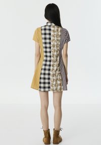 Vestido de manga corta con un diseño de patchwork que presenta varios patrones de cuadros en amarillo, negro y marrón. Tejido texturizado, forma ajustada.