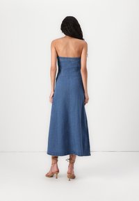 Denim maksi obleka s prilegačim korzetom in ravnim krilom. Ima brezramensko zasnovo ter diskretne šive. Barva je srednje modra.