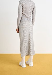 Grå, ribbad stickad uppsättning bestående av en tajt långärmad topp och en matchande lång kjol. Utsmyckad med ett våg-liknande mönster och tillsammans med vita sneakers.