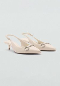 Tocuri slingback bej cu vârf ascuțit, prezentând un detaliu strălucitor cu cataramă argintie și un toc kitten de înălțime mică. Textură netedă, design minimalist.