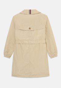 Beige trenchcoat med krave, elastiske manchetter, bælte i taljen og knapdetalje bagpå. Fremstillet af let, tekstureret stof.