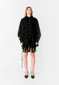 Vestido camisón negro de gran tamaño con botones en el frente, con tirantes de patchwork y detalles de flecos. Tejido elegante con una textura suave.