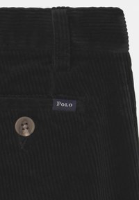 Black corduroy pants featuring a button closure and a "Polo" label near the pocket. The fabric has a distinctive ridged texture.
