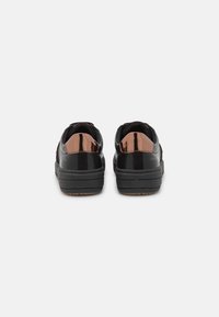 Zapatillas negras con un acento marrón brillante en el talón, textura suave, forma redondeada y suela de goma gruesa para mayor soporte.