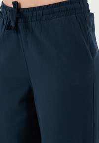 Marineblauwe elastische broek met taillekoord, voorzien van zijzakken en een textuurstof voor comfort en duurzaamheid.
