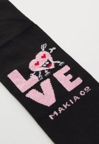 Calzino nero con grande testo rosa che spellano "LOVE," arricchito da un personaggio a forma di cuore con occhi e denti, completando il design.