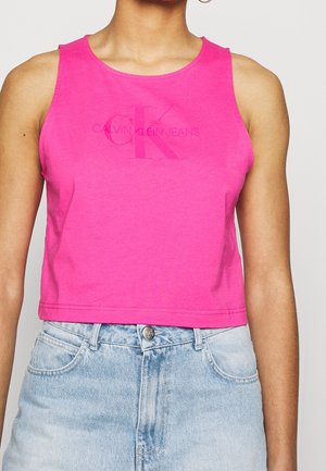 Femme portant un crop top sans manches rose vif avec le logo "Calvin Klein Jeans" et un jean taille haute bleu clair.
