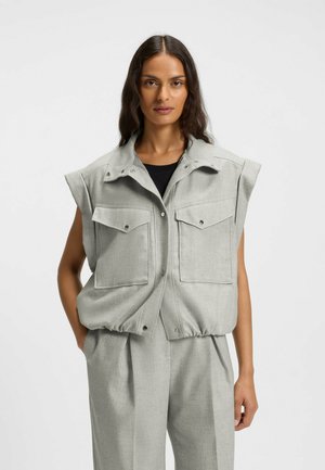 Hellgraue ärmellose Weste aus strukturiertem Stoff mit zwei Brusttaschen, Druckknöpfen und einem elastischen Saum. Kombiniert mit passender Hose.