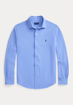 Hellblaues, langärmliges Hemd mit Knopfleiste, Kragen und kleinem dunklem Logo auf der linken Brust, flach auf weißem Hintergrund präsentiert.