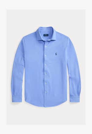 Jasnoniebieska koszula na guziki z długim rękawem, kołnierzykiem i małym ciemnym logo na lewej piersi, prezentowana na płasko na białym tle.