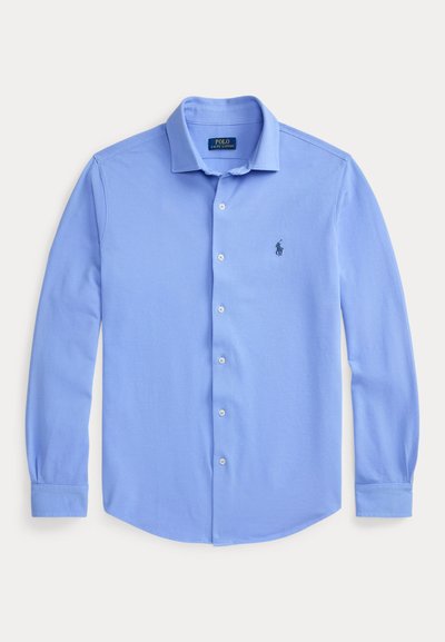 Ανοιχτό μπλε πουκάμισο με μακριά μανίκια, κουμπιά και γιακά, με μικρό σκούρο λογότυπο στο αριστερό στήθος, απλωμένο επίπεδα πάνω σε λευκό φόντο.