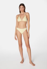 Twee-delige bikini set in zacht geel, met een getextureerde driehoekstop met halterbandjes en een bijpassende middenhoogte onderbroek met een naadloze afwerking.