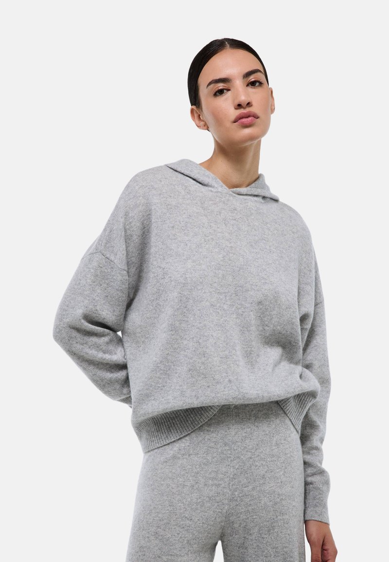 Haut à capuche en maille grise avec une texture douce, coupe décontractée, ourlet côtelé et capuche à cordon, associé à un bas gris assorti.