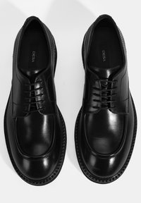 Schwarze Lederschuhe mit glatter Oberfläche, runder Zehenform und Schnürdesign. Gestickte Akzente und eine strapazierfähige Sohle runden das Design ab.