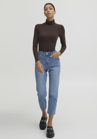 Top de cuello alto marrón de manga larga, jeans de tiro alto azul claro, cortos a los tobillos, combinados con mocasines negros y accesorios mínimos.