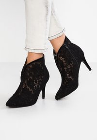 Bottines en dentelle noire avec des bouts pointus, des talons hauts et une fermeture éclair. Présentent des motifs floraux et un tissu texturé.