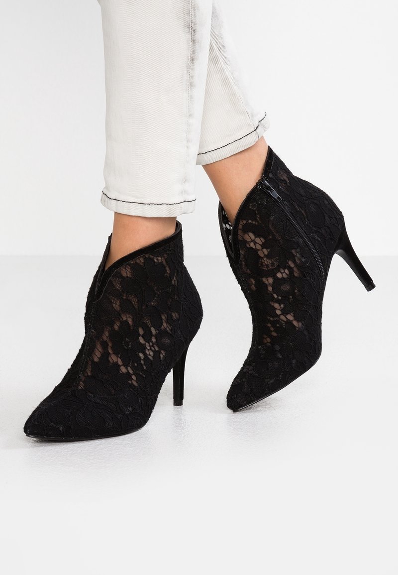 Bottines en dentelle noire avec des bouts pointus, des talons hauts et une fermeture éclair. Présentent des motifs floraux et un tissu texturé.