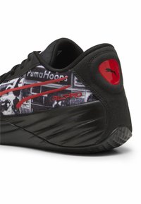 Scarpa sportiva nera con suola nera testurizzata. Presenta un motivo grafico con accenti rossi, logo sul tallone e design elegante.