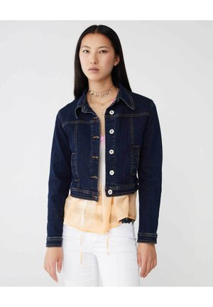 Giubbotto di jeans blu scuro con design cropped, colletto classico, chiusura anteriore con bottoni e cuciture a contrasto. Indossato sopra un top leggero a strati.