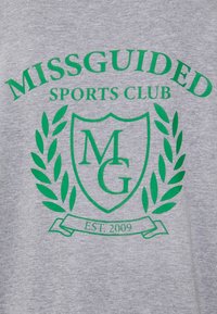 Šedé tričko s zeleným grafickým designem. Obsahuje text "MISSGUIDED SPORTS CLUB" a štít s iniciály "MG", obklopený vavřínem.
