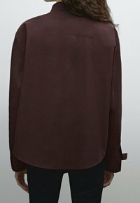 Chemise bordeaux à manches longues avec un col pointu, des poignets à boutons et une texture lisse. Design simple sans motifs ou accents supplémentaires.