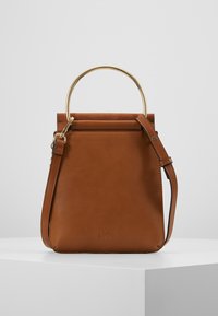 Ruskea nahkainen käsilaukku, jolla on jämäkkä muoto, kultainen pyöreä kahva, säädettävä hihna ja sileä pinta. Huomaamaton logo-yksityiskohta.