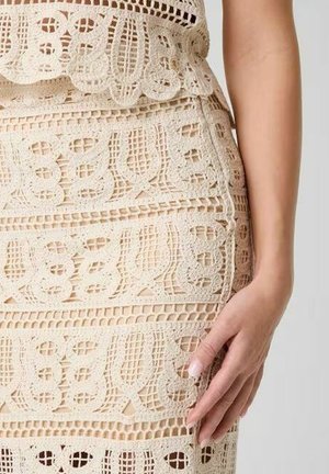 Vestito beige all'uncinetto con intricati motivi in pizzo, che mostra il busto di una donna e la sua mano che riposa dolcemente sul fianco.