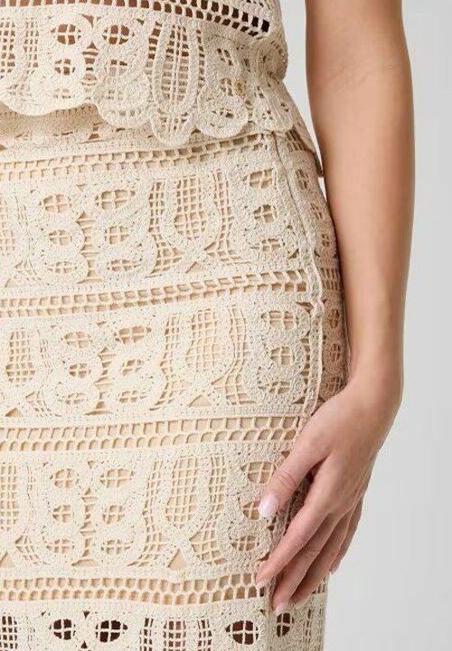 Robe en crochet beige avec des motifs de dentelle complexes, montrant le torse d'une femme et sa main reposant doucement sur sa hanche.