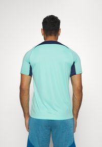 Camiseta deportiva de manga corta en azul claro con detalles en azul marino, que presenta un patrón texturizado en los hombros y una tela suave, diseñada para el rendimiento.