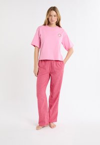 Roze katoenen t-shirt met korte mouwen en een ronde logo, gecombineerd met loszittende, gestructureerde rode geruite pyjamabroek.